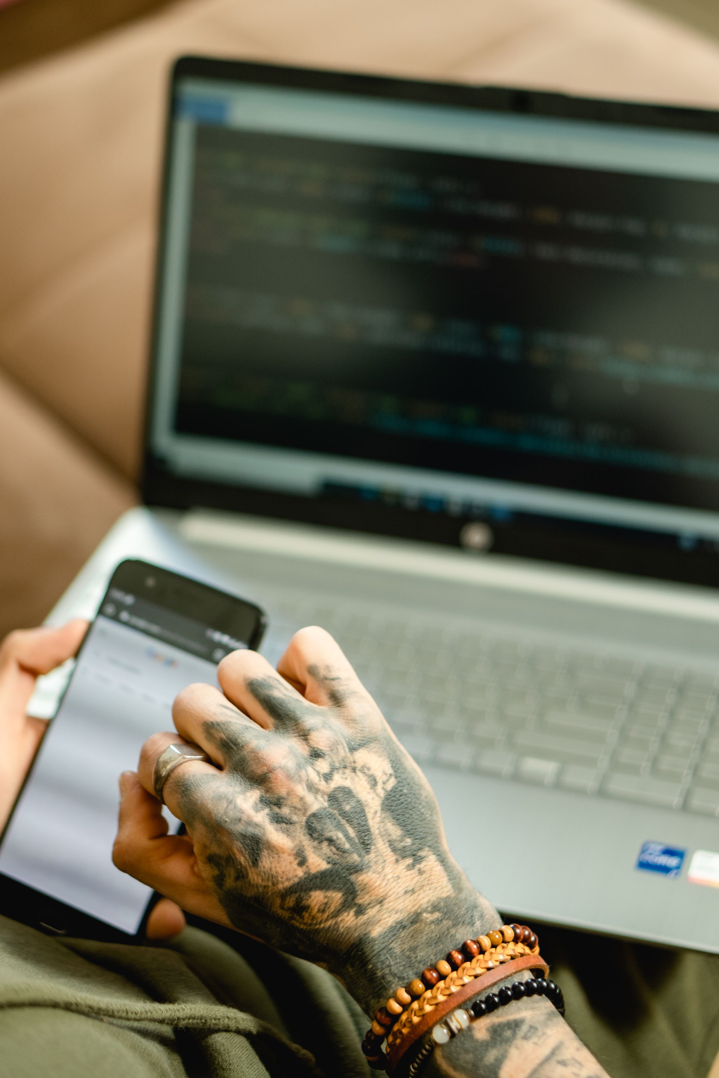 Mão com tatuagem ao lado de notebook com código em ambiente tech